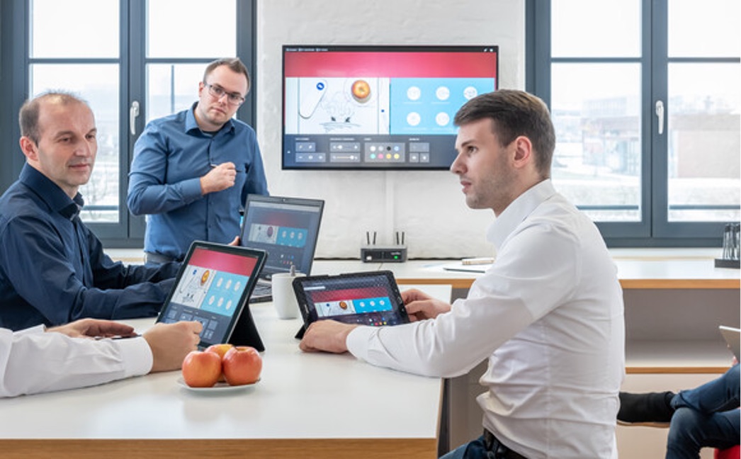 Team im Besprechungsraum arbeitet mit Tablets und einem großen Wanddisplay